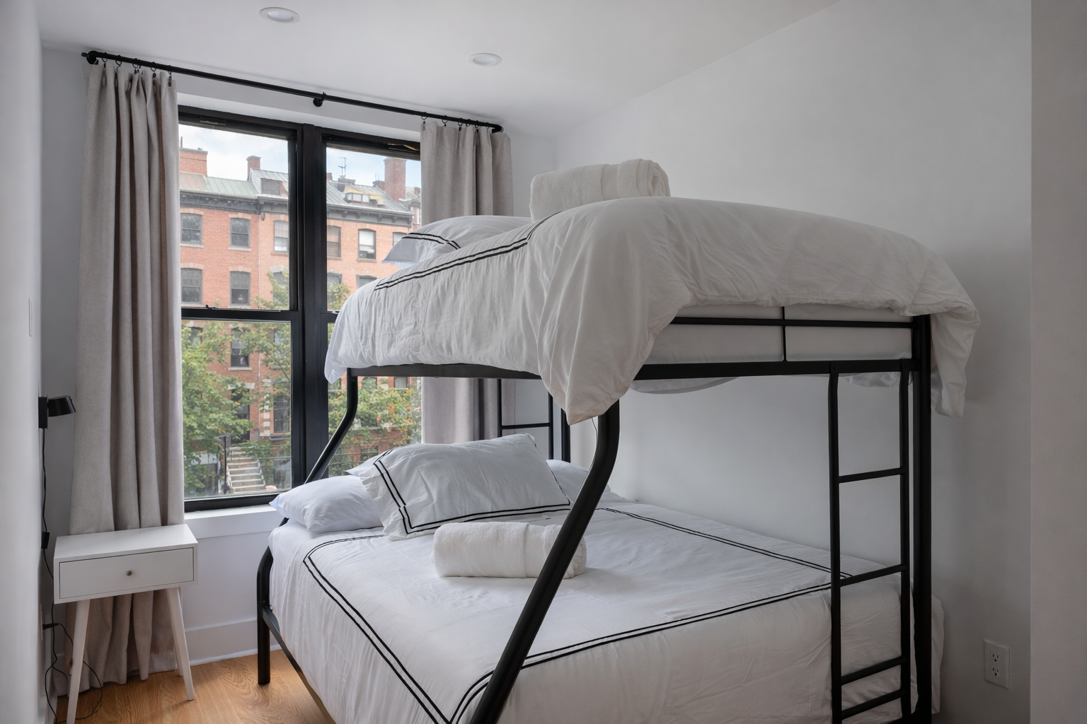 Bunk room with a black twin-over-full bunk bed and a window onto brick row houses