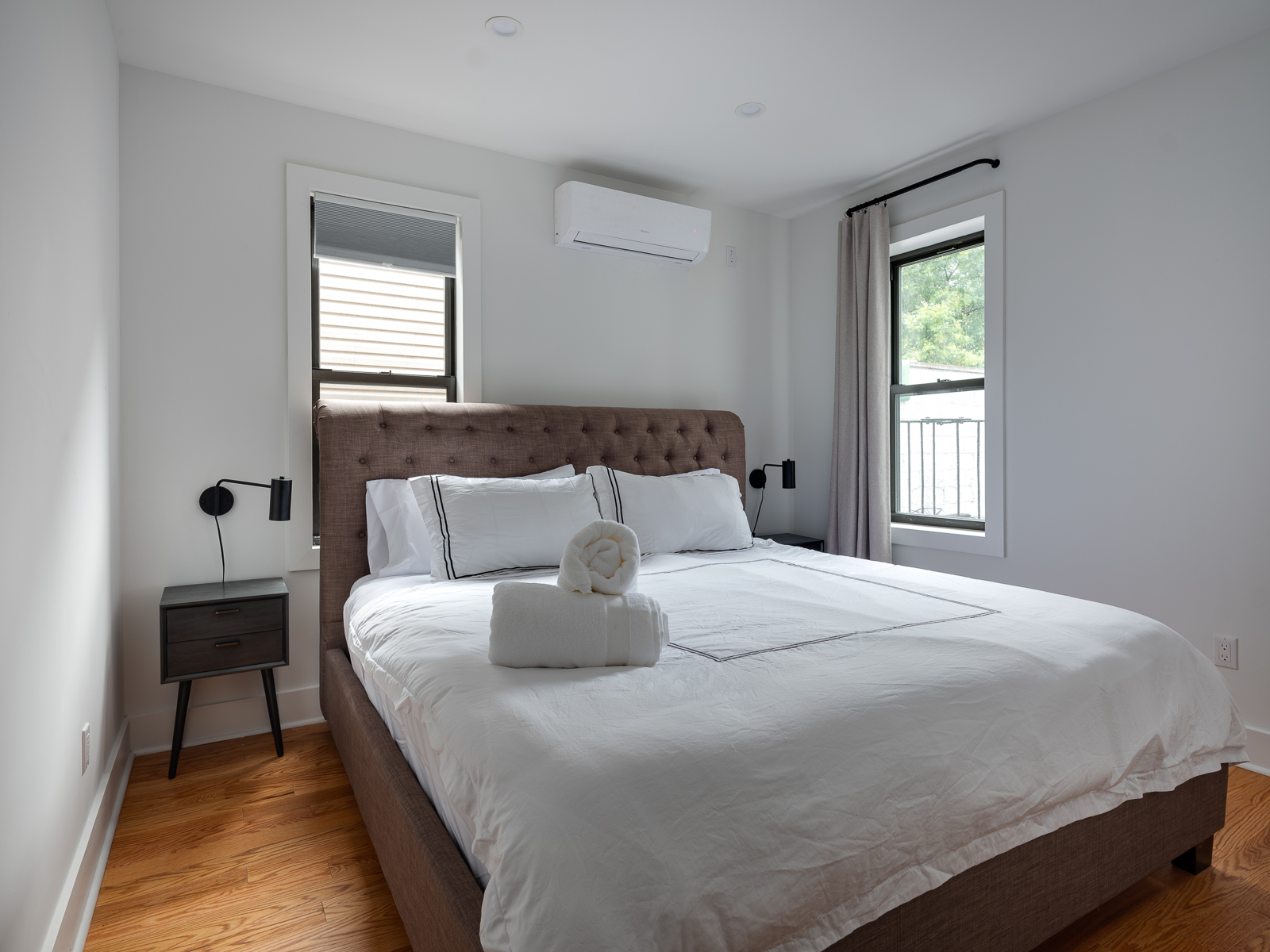 King bedroom with tufted headboard, white linens and black reading sconces
